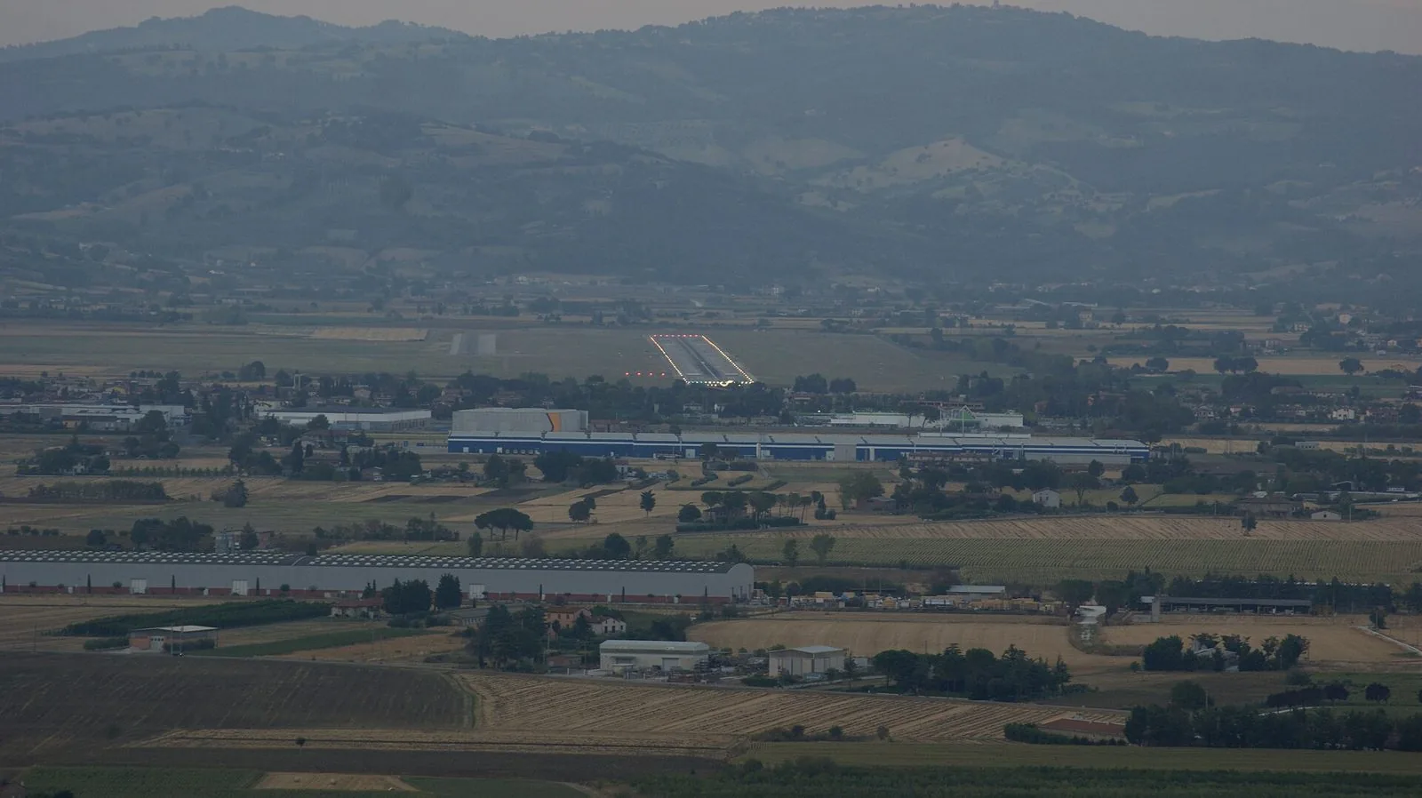 Vista dall'alto della piana di Sant'Egidio con la pista illuminata dell'aeroporto di Perugia e le colline sullo sfondo
