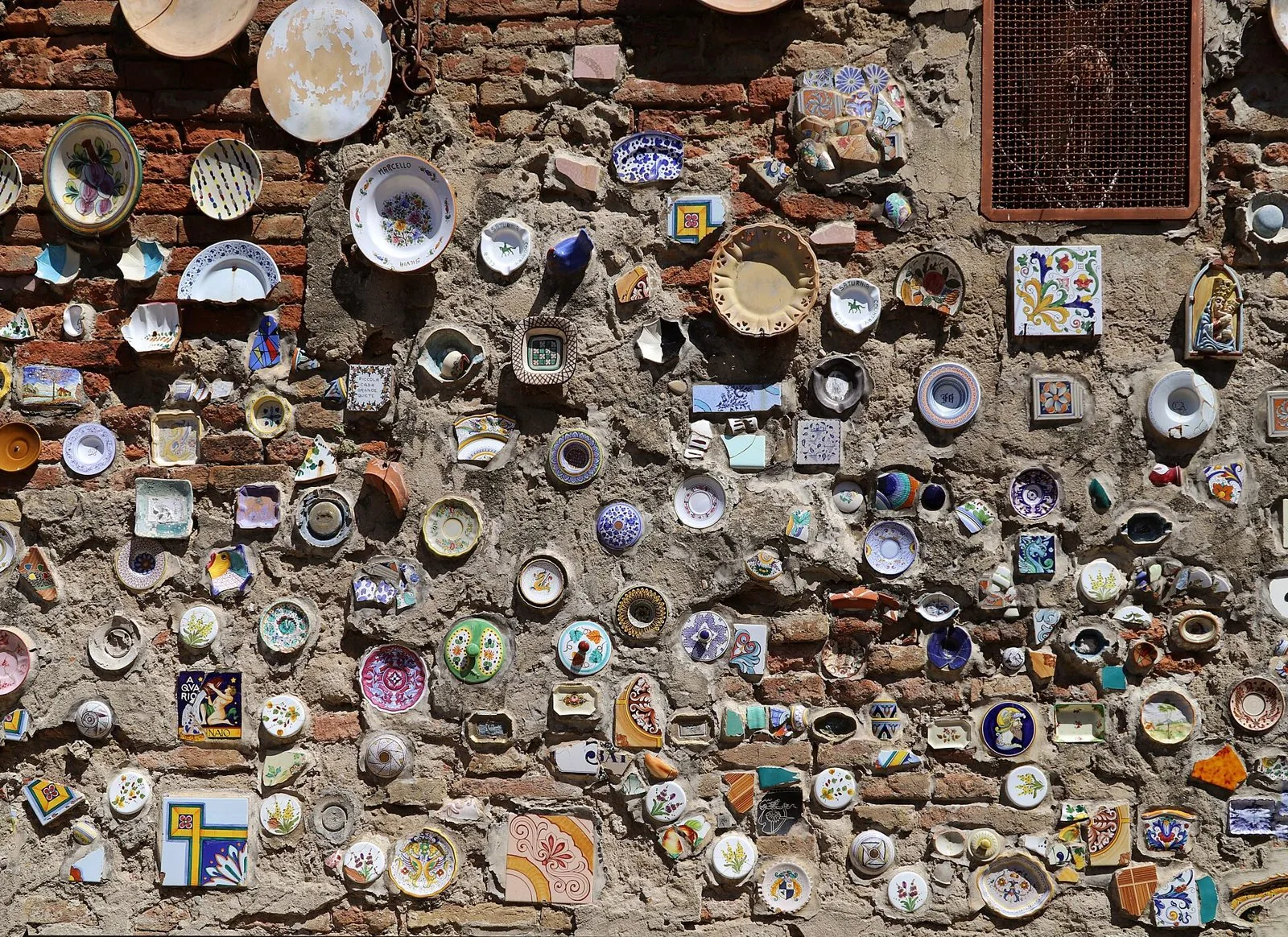 Un muro di mattoni a Deruta decorato con piatti, piastrelle e frammenti di ceramica dipinta di molti colori