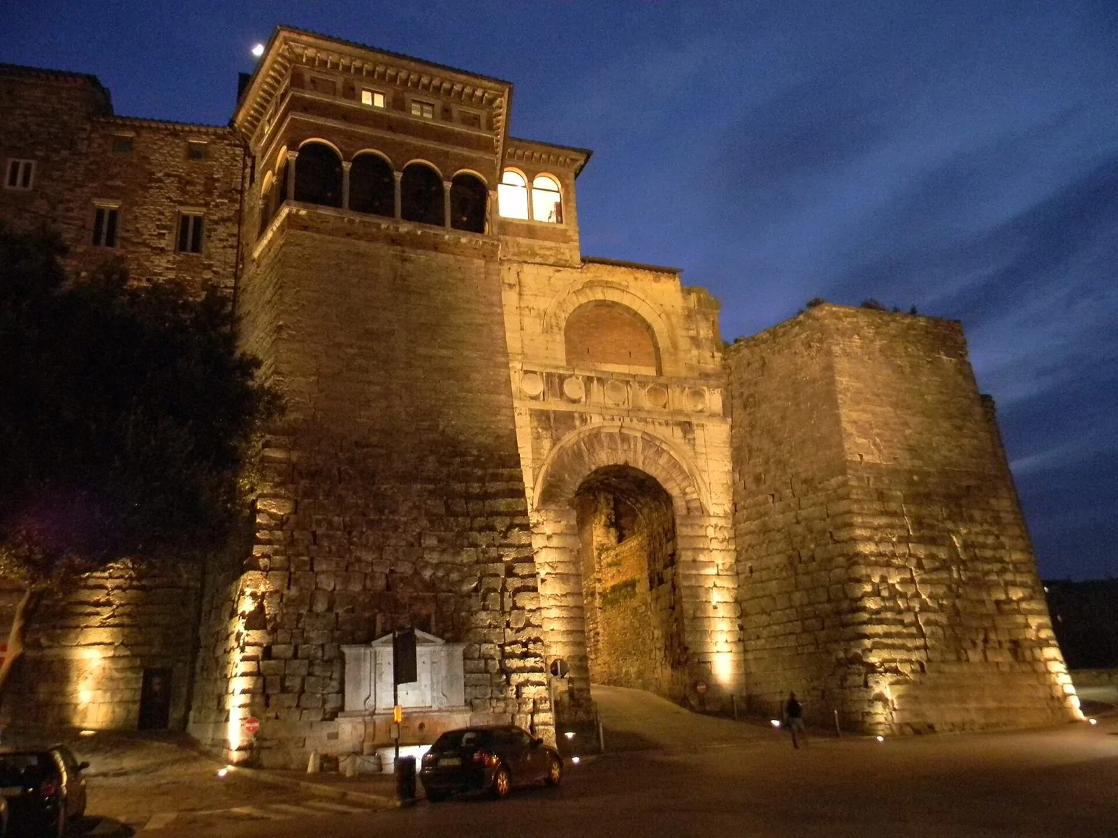 L'Arco Etrusco di Perugia illuminato al crepuscolo, con la loggia rinascimentale sulla torre e le grandi mura in blocchi di pietra